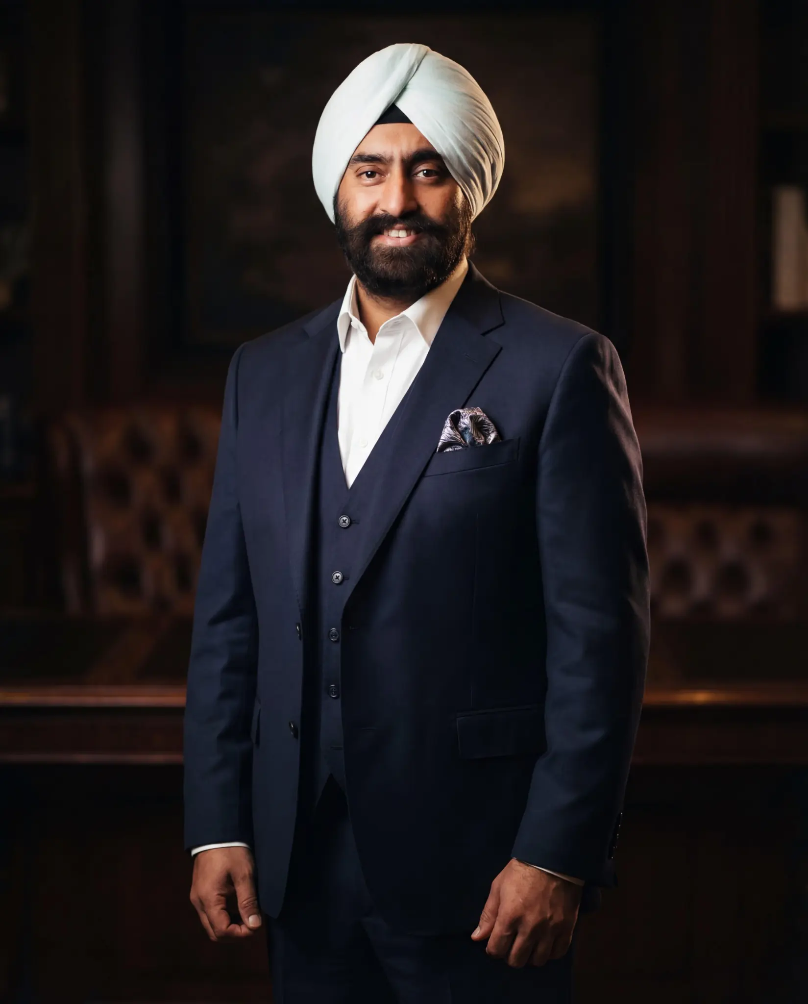 Dr. Jasdip Singh Jesse in a navy three-piece suit in a refined interior